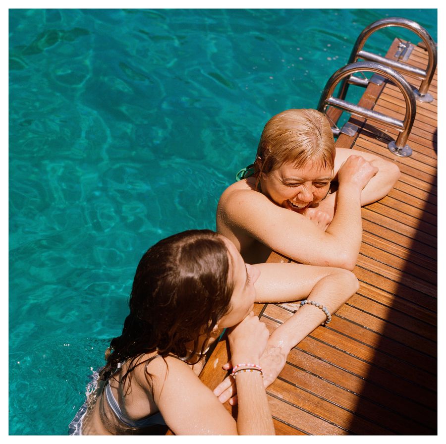 Two friends laughing in turquoise water beside the deck of the boat
